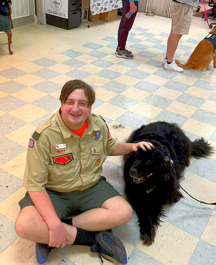 Patrick Joseph Corr III in his Scout uniform, sitting with a black Newfoundland service dog at a VetPets event